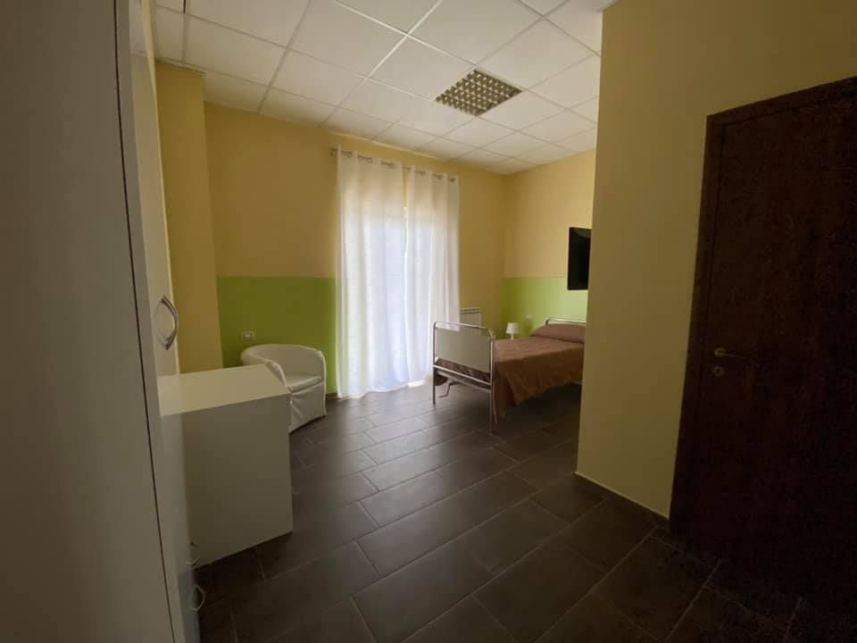 Stanza da letto con finestra, pavimenti in legno scuro e pareti dai colori neutri.
