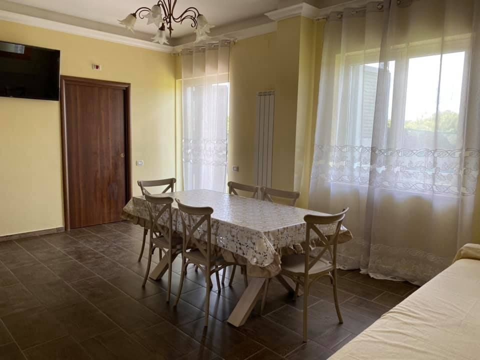 Sala da pranzo con tavolo, sedie, finestre con tende e TV a parete.