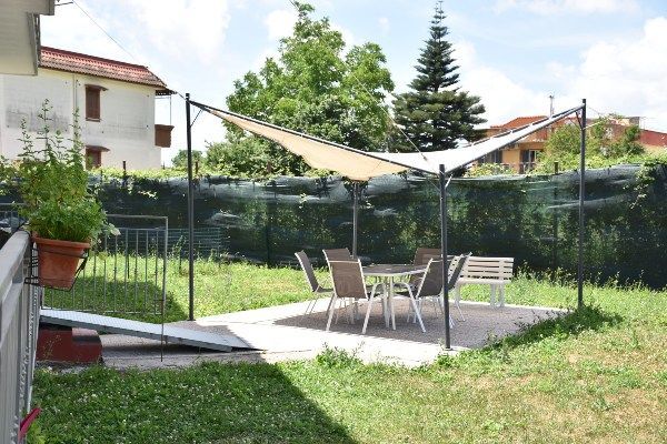Patio esterno con tavolo, sedie e tenda parasole in un giardino erboso.