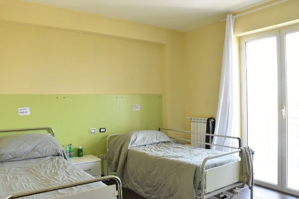 Due letti in una stanza con una finestra e pareti gialle/verdi.