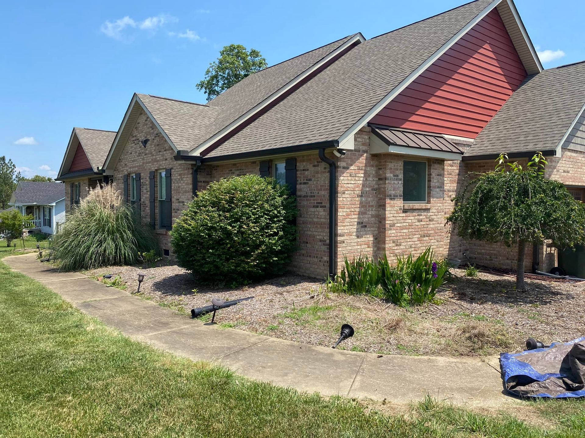 A large brick house with a red roof and a blue tarp in front of it.