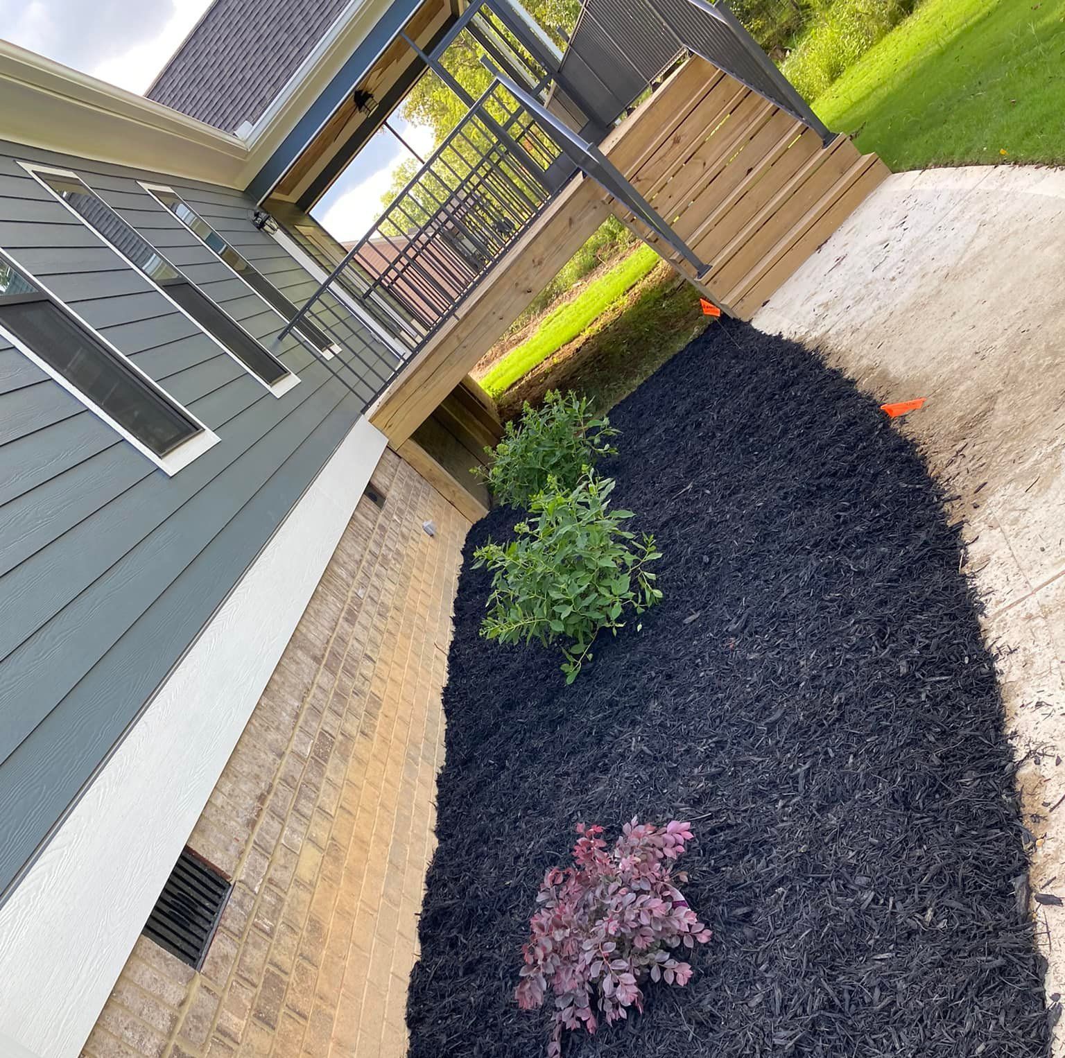 A yard with black mulch and plants in front of a house