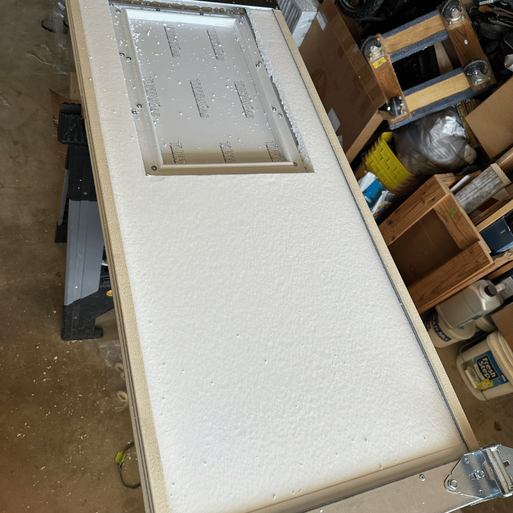 A door panel with white foam insulation and a rectangular inset frame, resting on a workshop sawhorse.