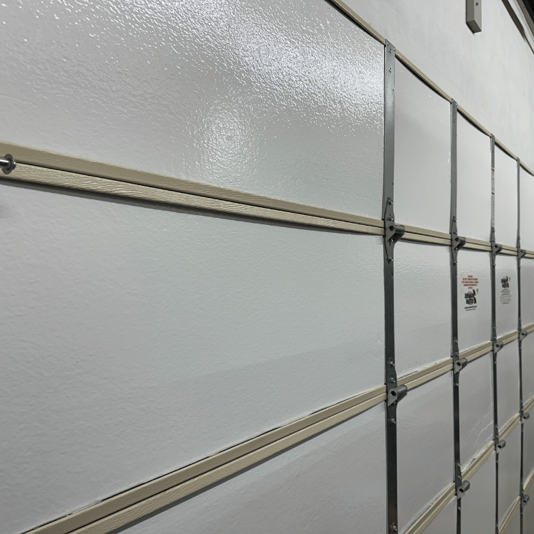 A side-view close-up of a white residential garage door, showing horizontal panels and metal vertical hinges.