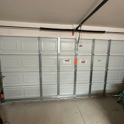 A closed white sectional garage door with metal vertical supports installed in a garage.