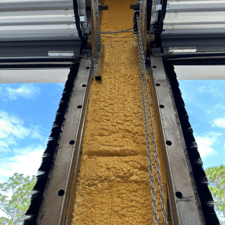A narrow, vertical view of spray foam insulation between metal garage door tracks, with blue sky visible on either side.
