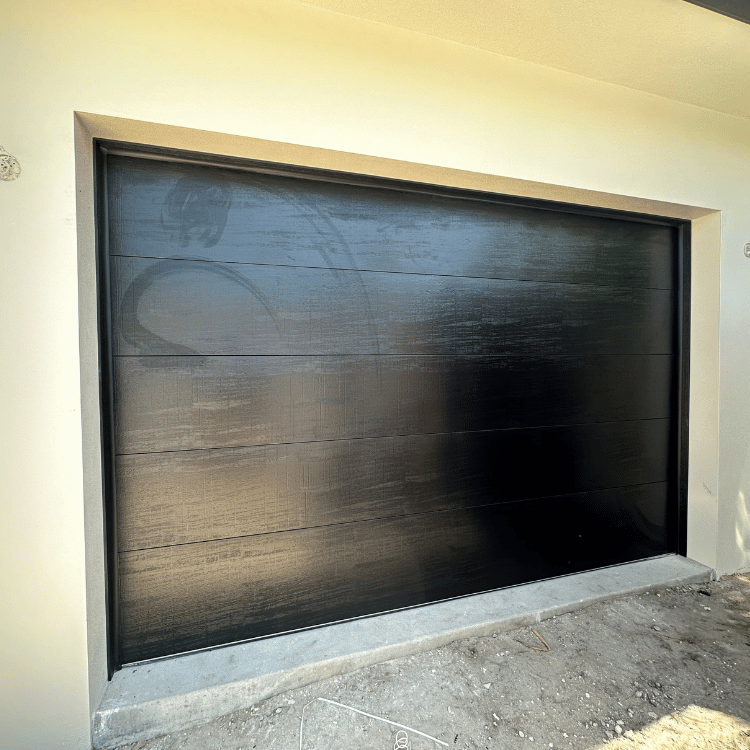 A modern, black, horizontal-paneled garage door installed in a light-colored stucco wall.