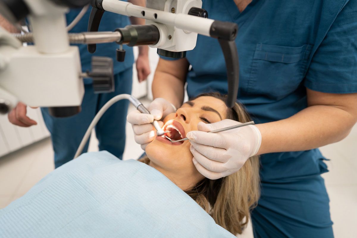 A woman is getting her teeth examined by a dentist using a microscope.
