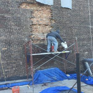 A man is working on a brick wall on a scaffolding.