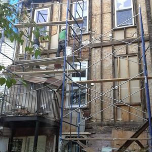 A man is standing on a scaffolding on the side of a building.