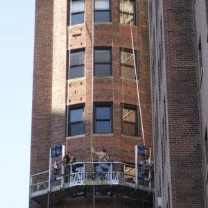 A group of people are working on the side of a tall brick building.