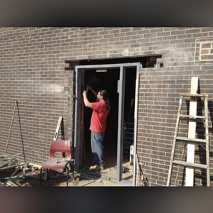 A man in a red shirt is working on a brick wall