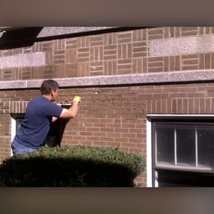 A man is working on a brick wall next to a window.