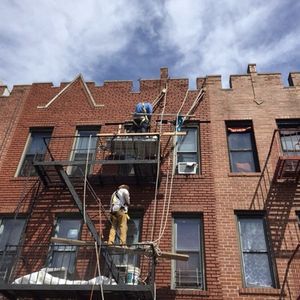 A man is standing on a fire escape on the side of a brick building.
