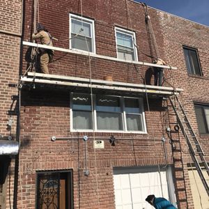 Two men are working on the side of a brick building.