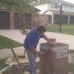 A man is working on a brick chimney in front of a house.