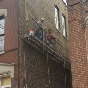 Two men are working on the side of a brick building