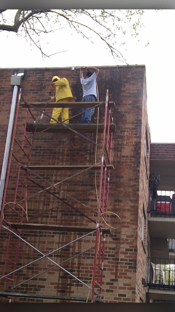Two men are standing on scaffolding on the side of a brick building.
