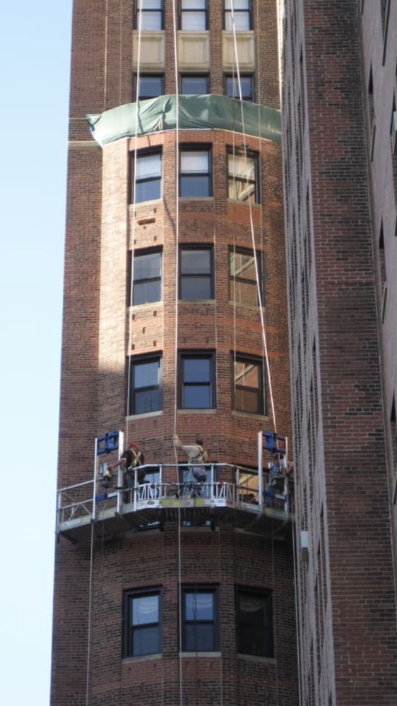 A brick building is being painted with a green tarp