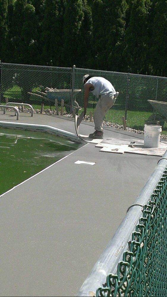 A man is painting a tennis court next to a fence.