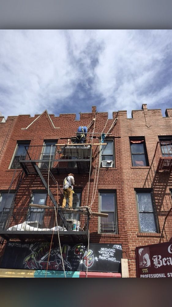 A man is standing on a scaffolding on the side of a brick building.
