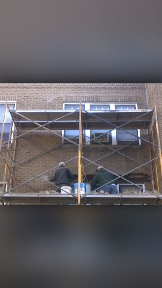 Two men are sitting on a scaffolding on the side of a building.