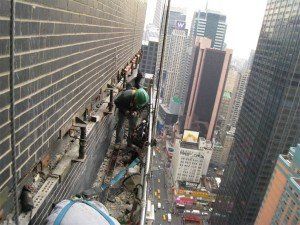 A man is working on the side of a building in a city.