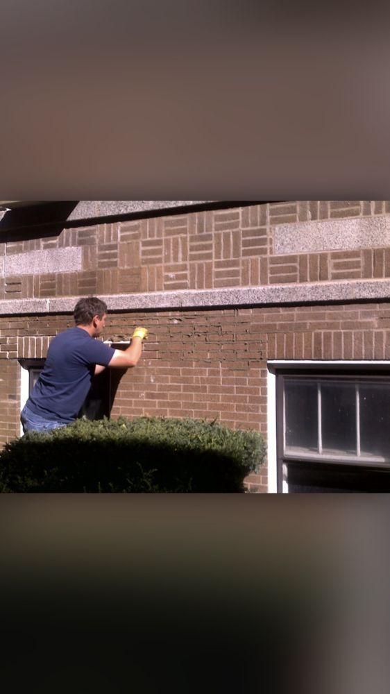 A man is working on a brick wall next to a window.