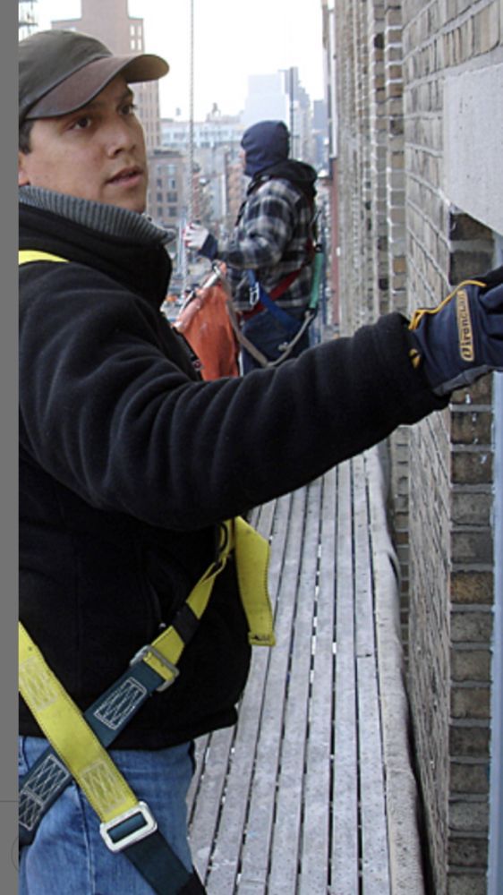 A man wearing a black jacket and blue gloves is working on a brick wall