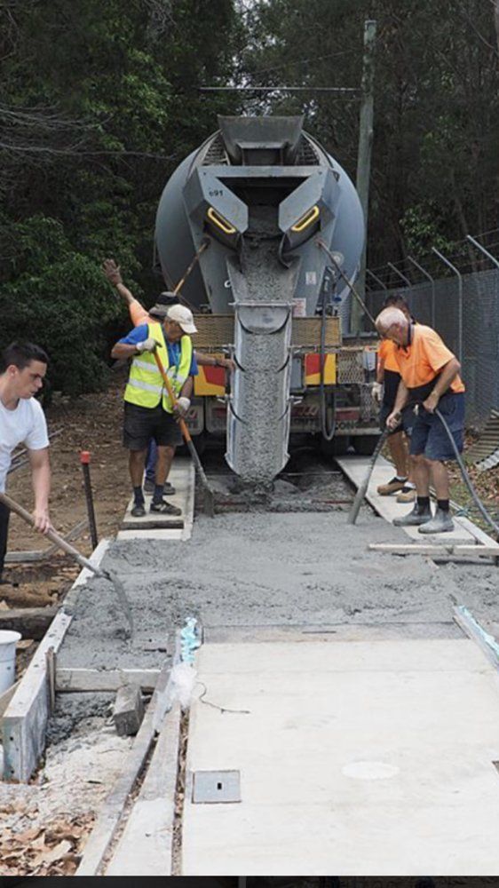 A group of construction workers are working on a sidewalk in front of a cement truck.