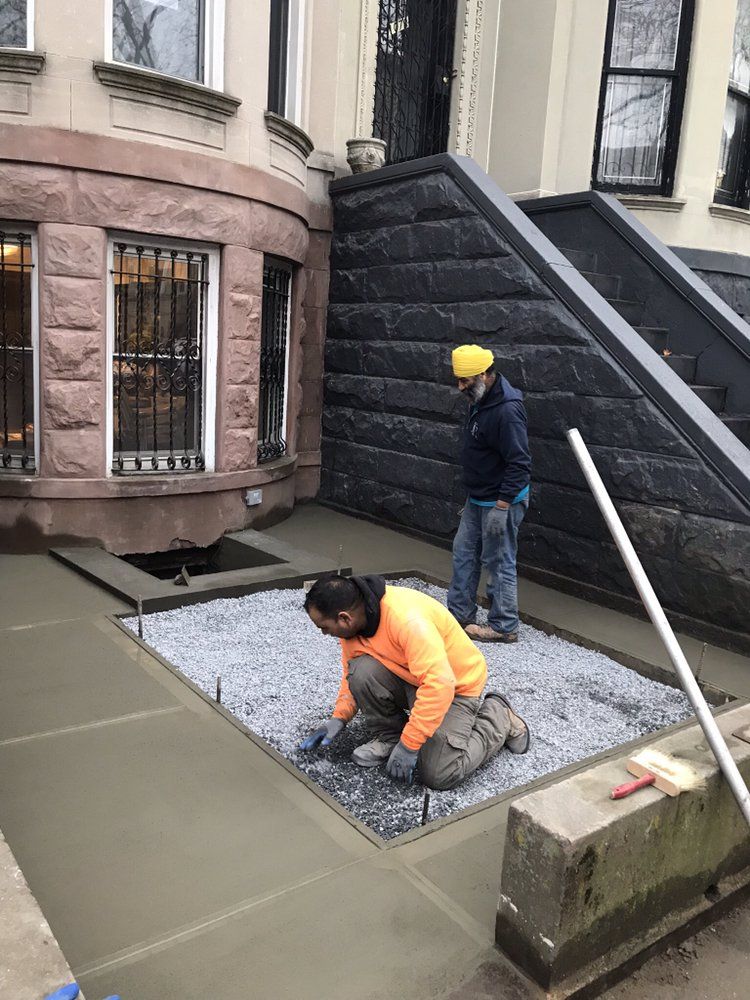 Two men are working on a concrete walkway in front of a building.