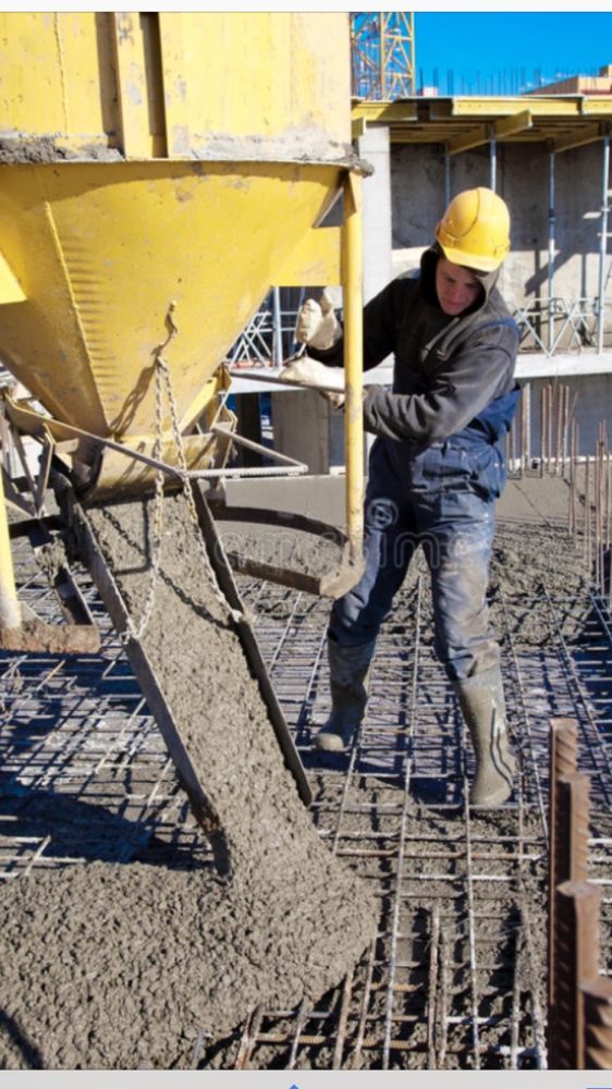 A man wearing a hard hat is pouring concrete on a construction site.