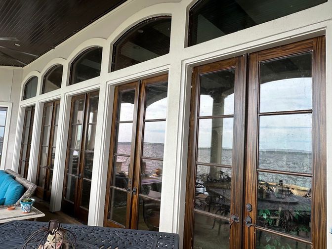 A person uses a handheld machine to clean a glass door, with a view of a lake and patio furniture in the background.