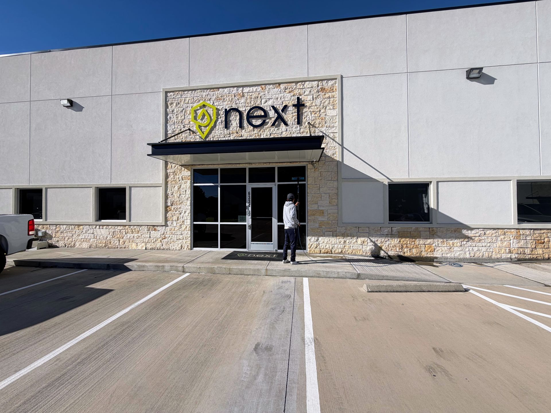 Storefront entrance with a “next” sign and a person standing by the doors on a sunny day