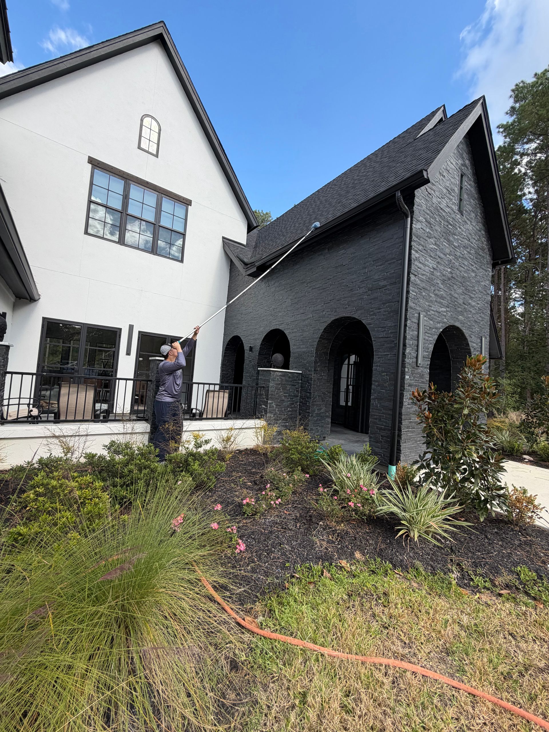 Modern white-and-black house with a landscaped front garden and a person standing outside