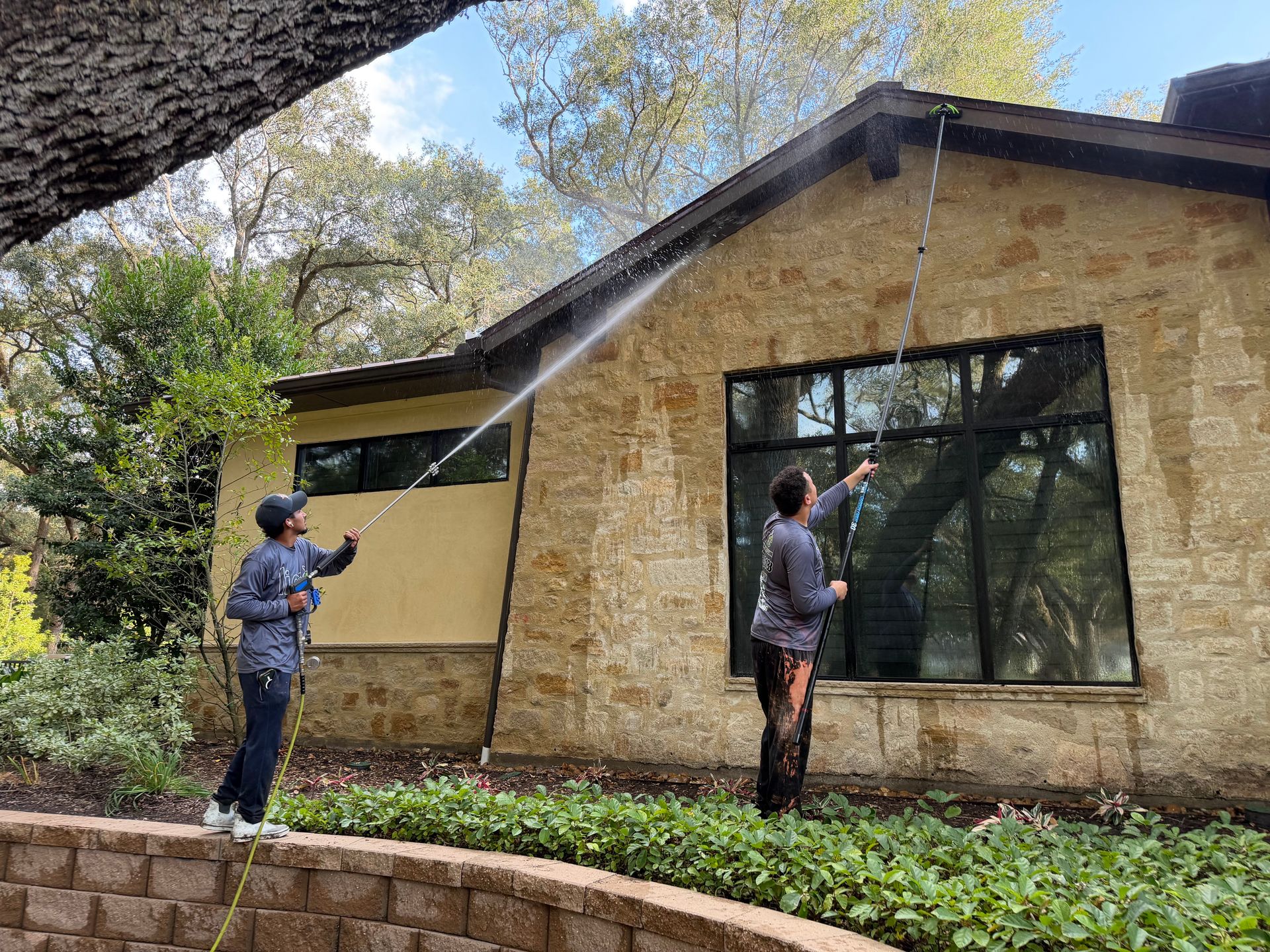 Two people using poles to measure a tan building exterior under trees