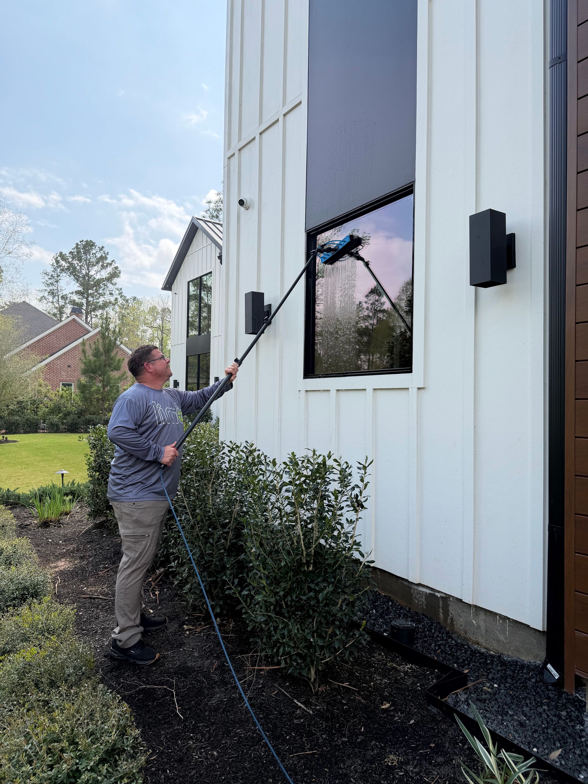 Person using a long brush to clean an upper window on a white building
