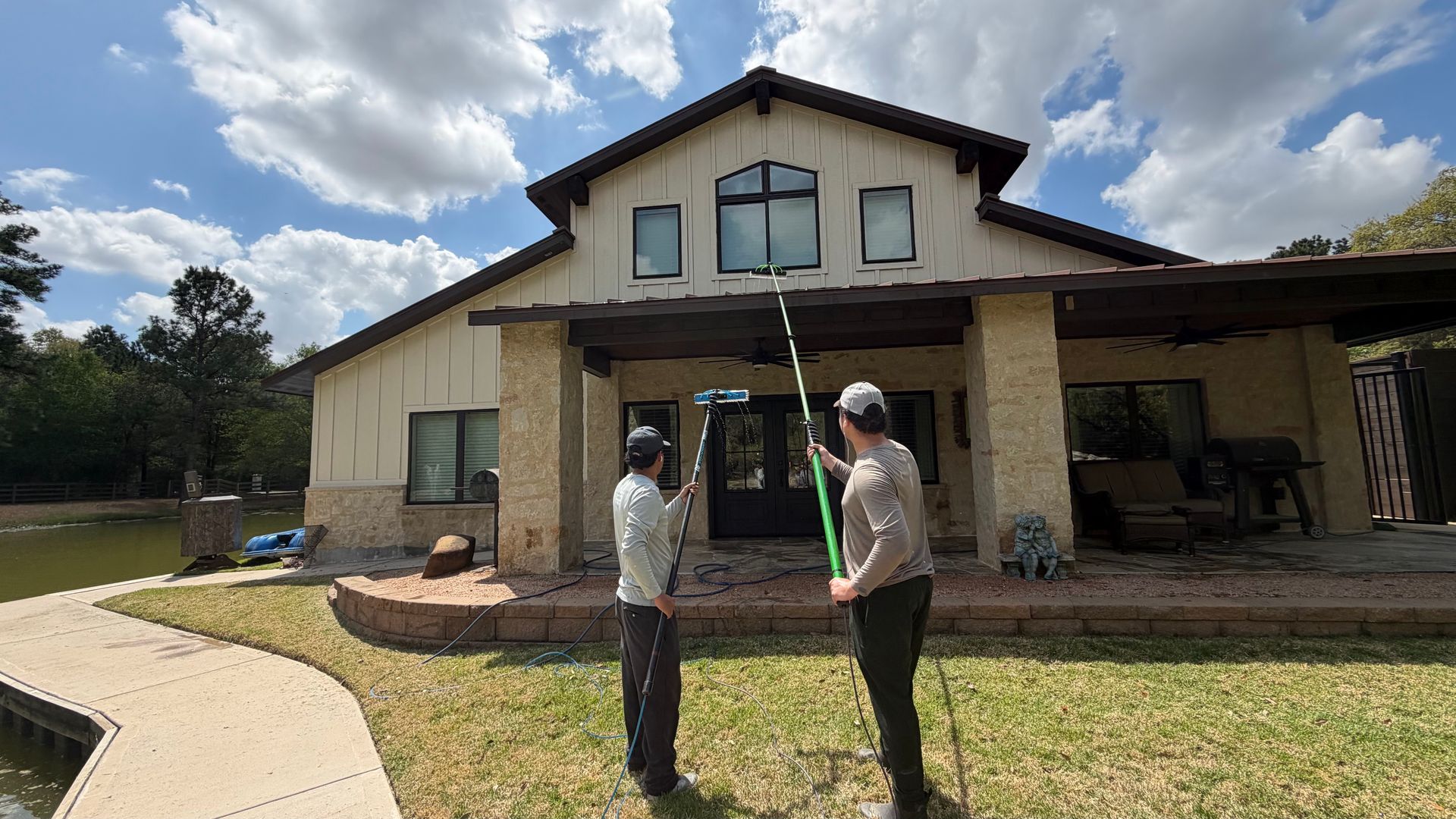 Two people stand outside a newly built house with stone columns and a covered porch under a partly cloudy sky.