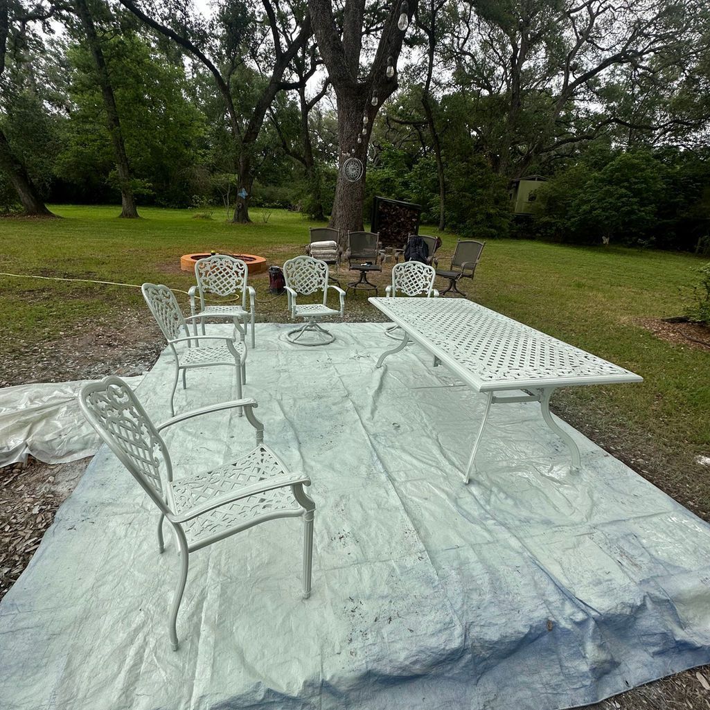 A white outdoor patio set featuring a table and four chairs sitting on a light-colored tarp in a grassy yard.