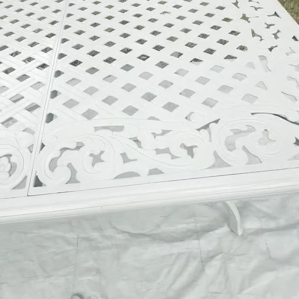 A white, metal outdoor table top featuring a lattice design and decorative, scrolling edges, sitting on a drop cloth.