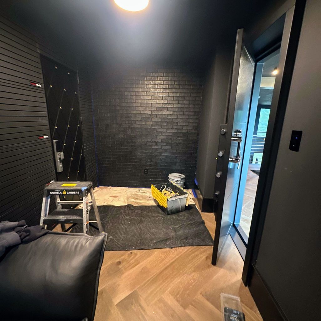 An interior view of a room under renovation with a dark brick wall, herringbone flooring, a step ladder, and tools.