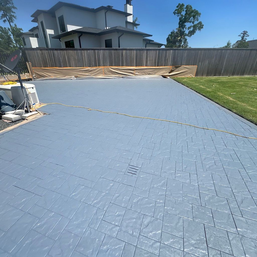 Light blue, interlocking grid tiles laid across a backyard patio next to a wooden fence and a house.