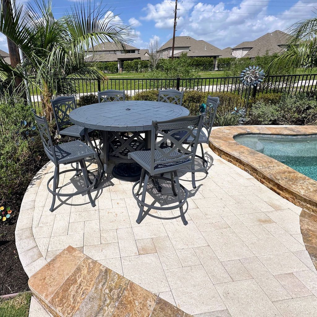 A wrought iron table and chairs on a paved patio beside a swimming pool, with houses in the background.