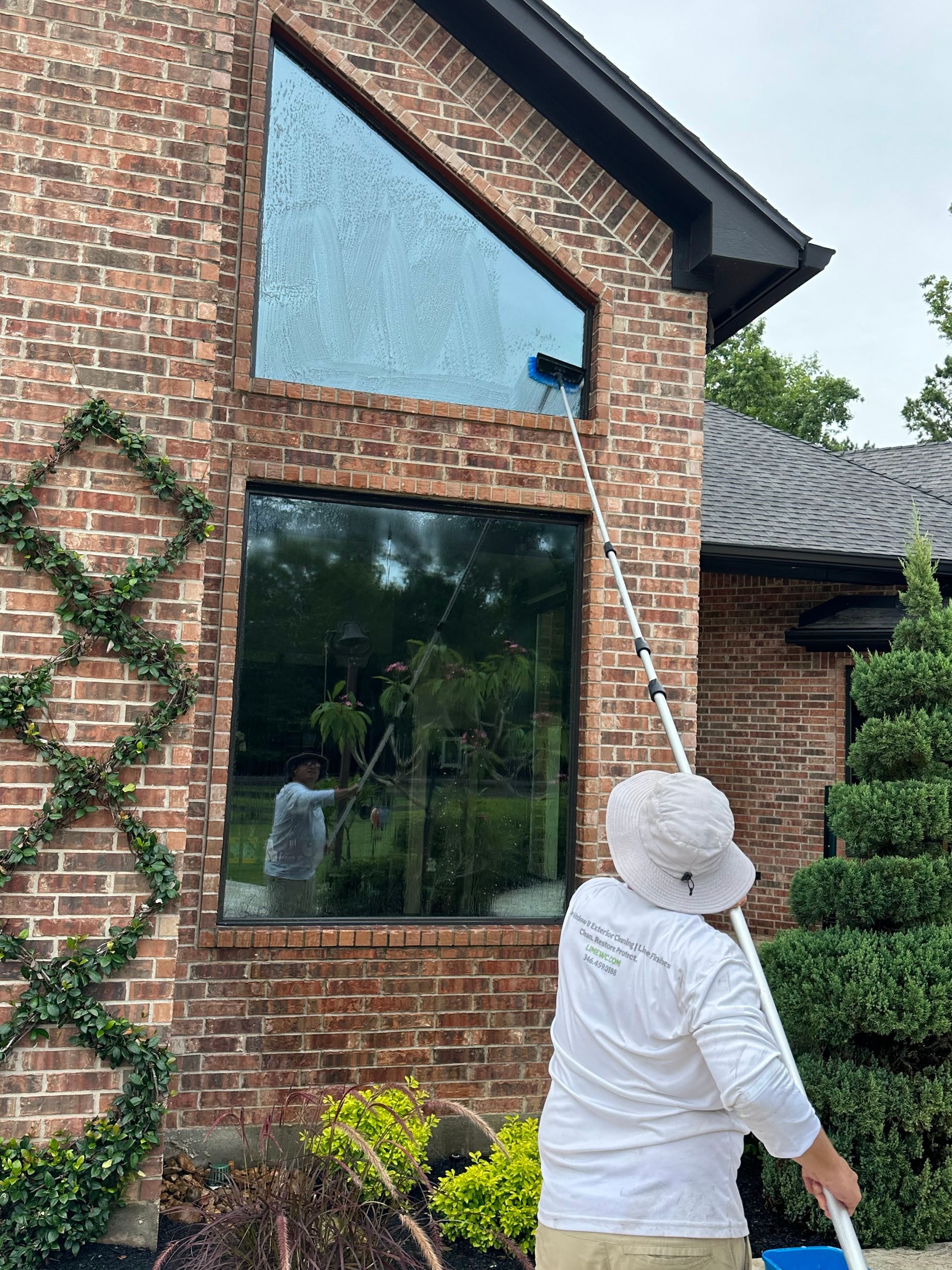 Person on a ladder cleaning a large window on a brick house with ivy accents