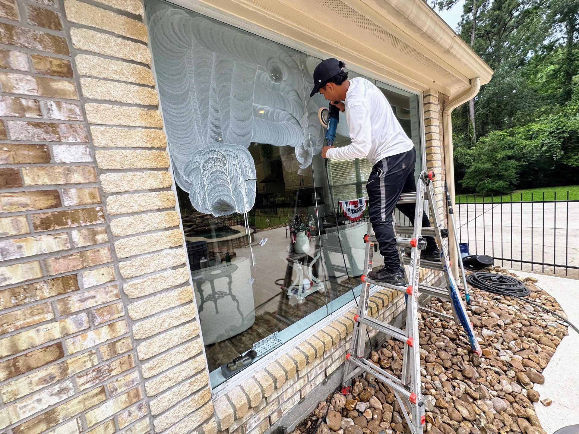 Worker on a ladder hanging lace curtains in a brick home’s front window.