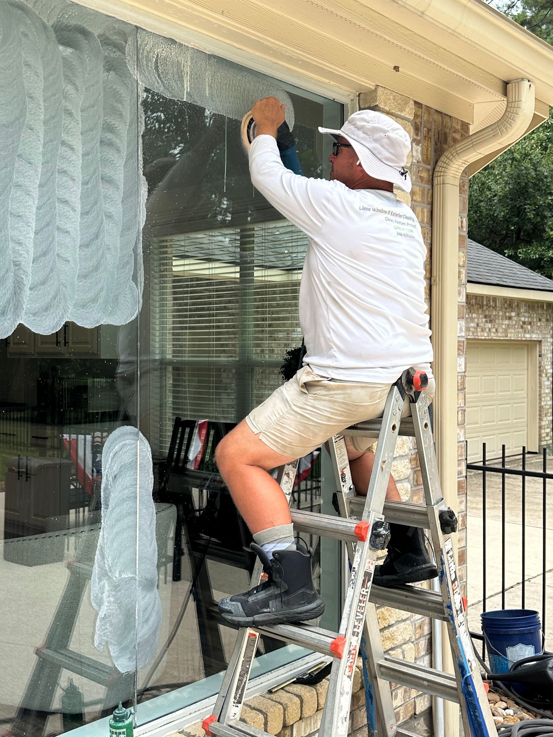 Person on a ladder cleaning a large window on a house exterior