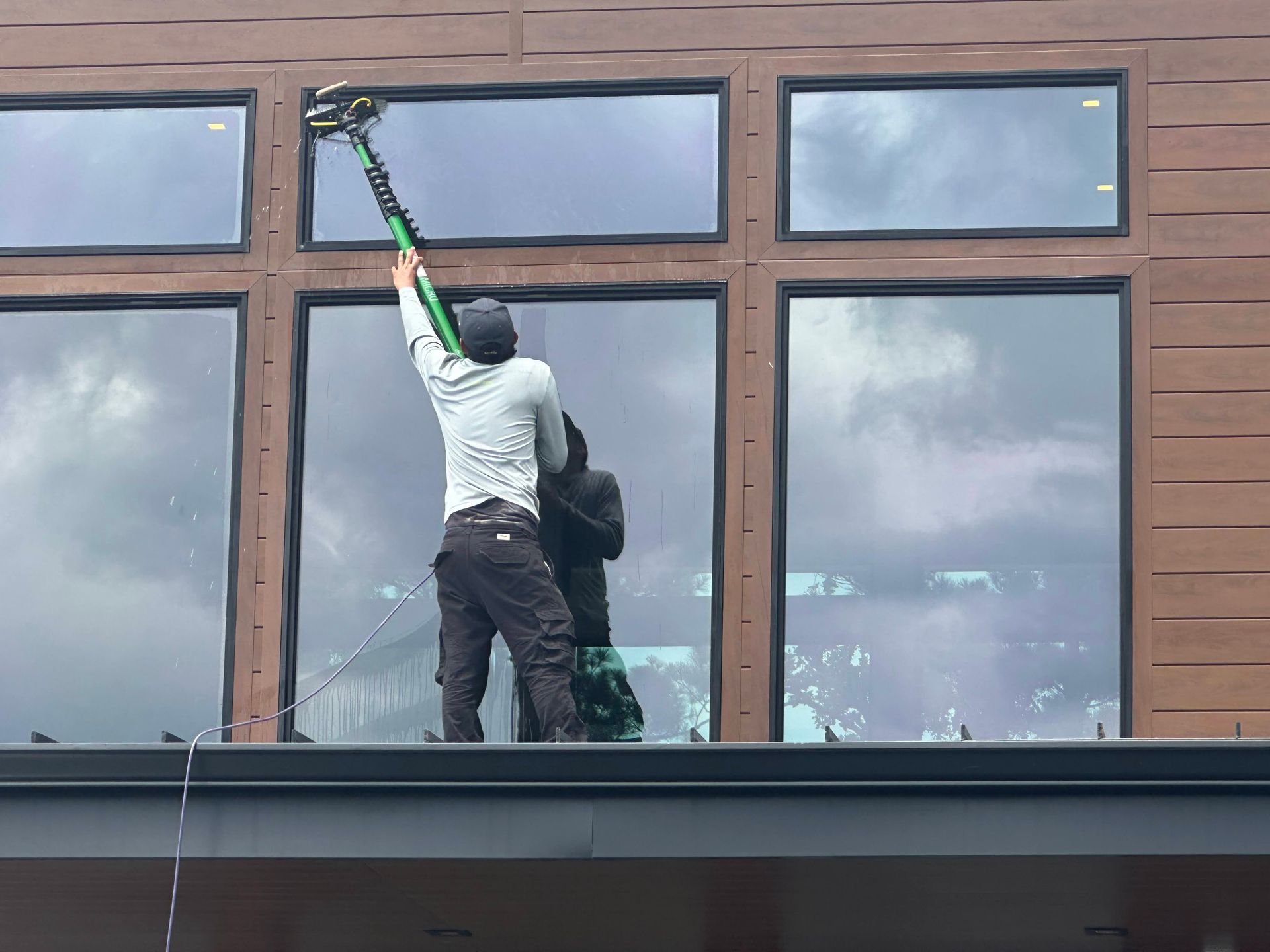 Worker cleaning a large window with a long pole on a building facade