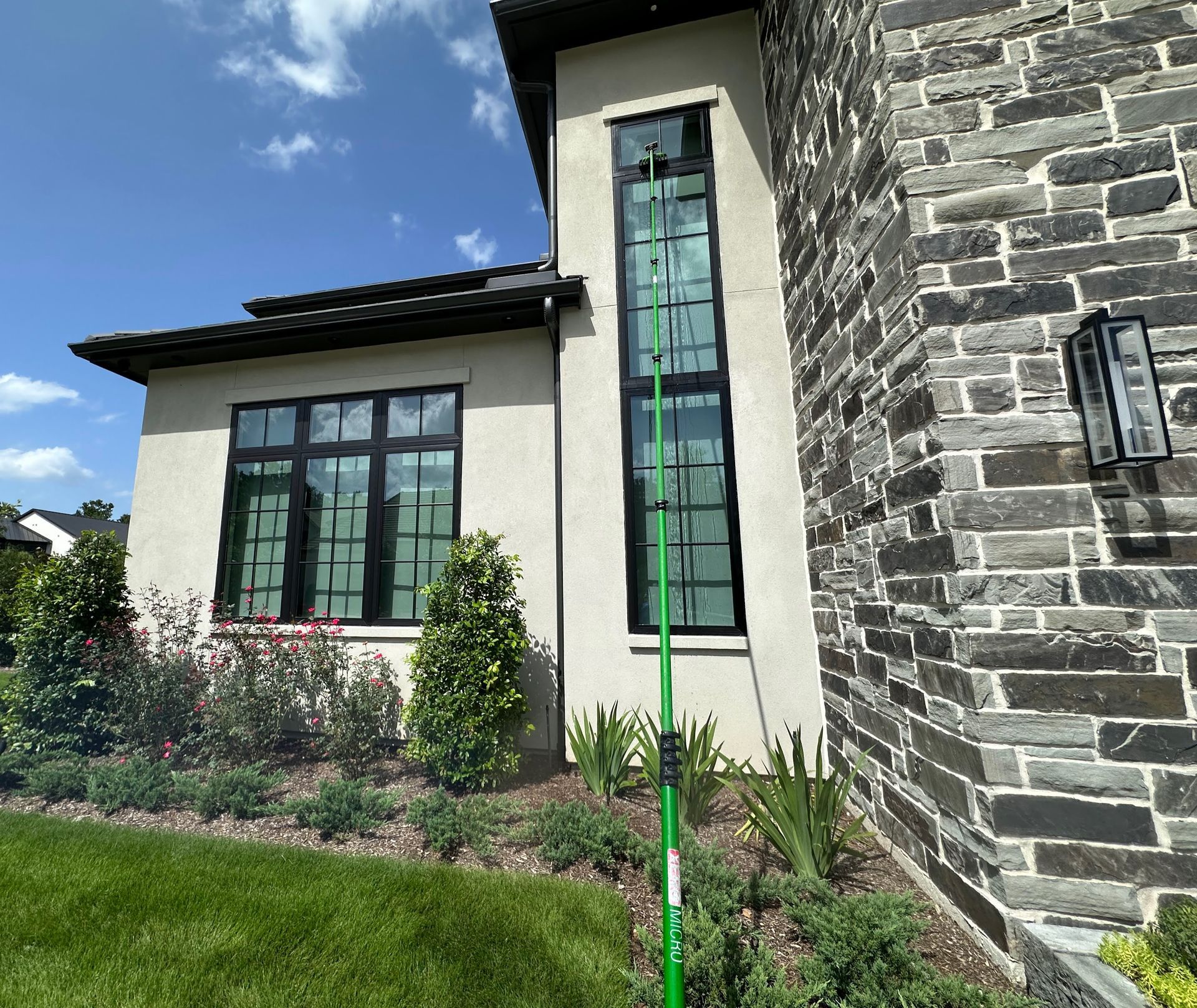 Modern house exterior with stone wall, large windows, and landscaped garden under a blue sky