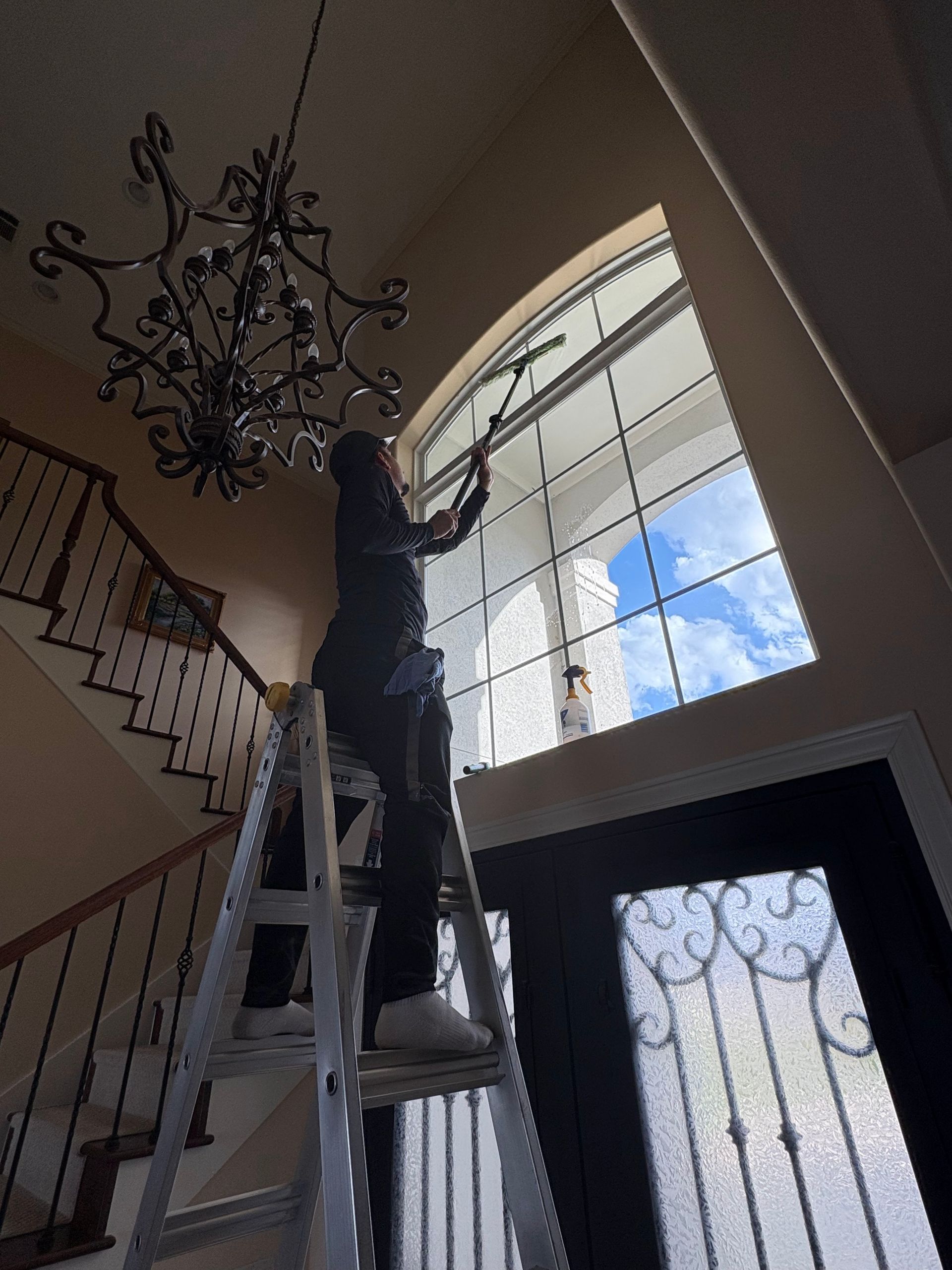 Person on a ladder cleaning a large arched window in a staircase foyer