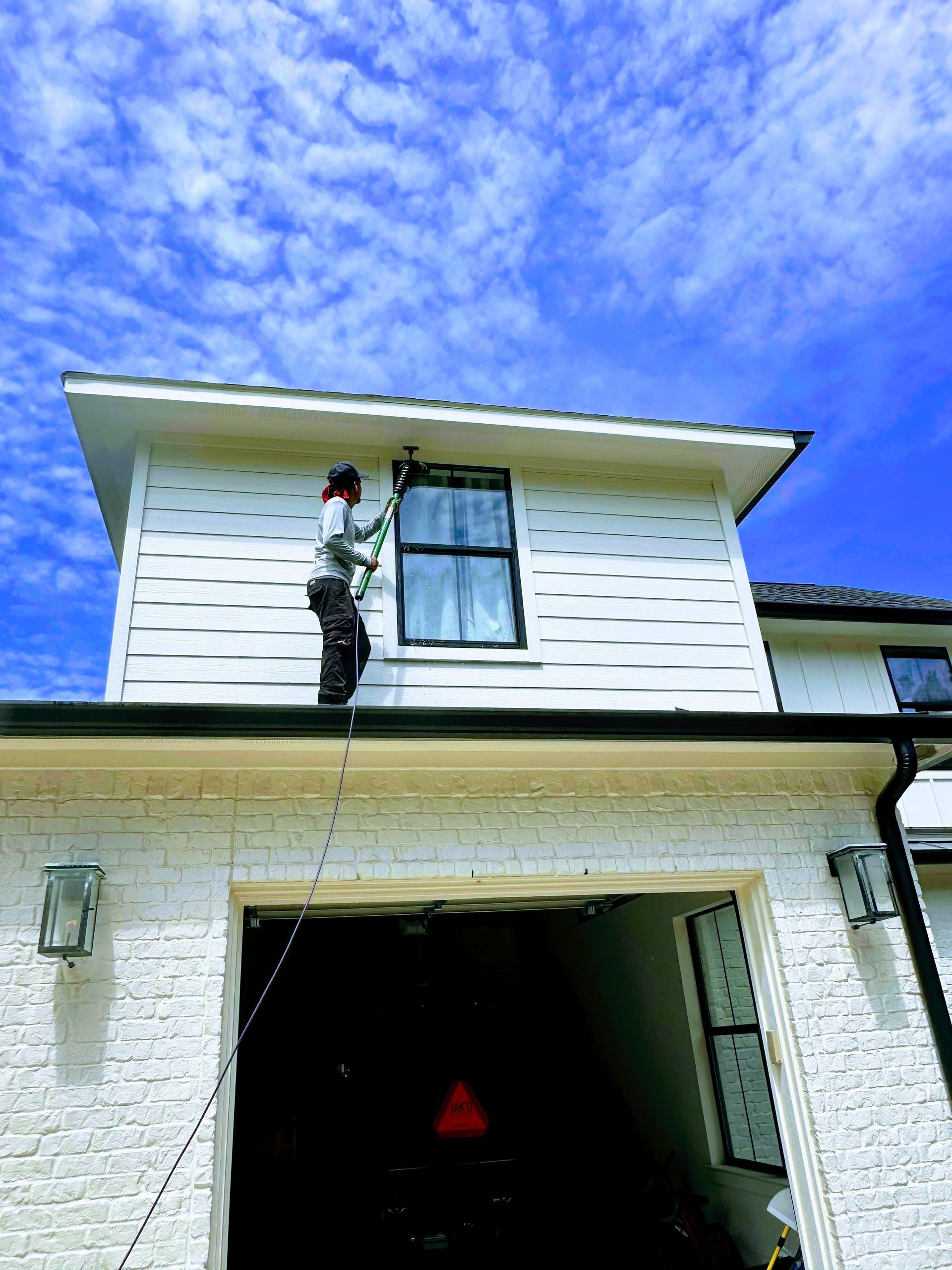 Person climbing a ladder to the second-story window of a white house beneath a bright blue sky